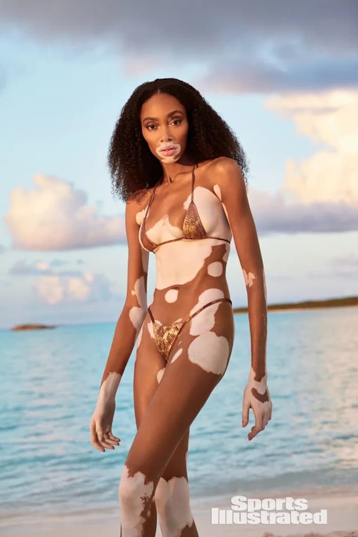Winnie Harlow stands on the beach and poses for the camera in a brown snake-printed bikini.